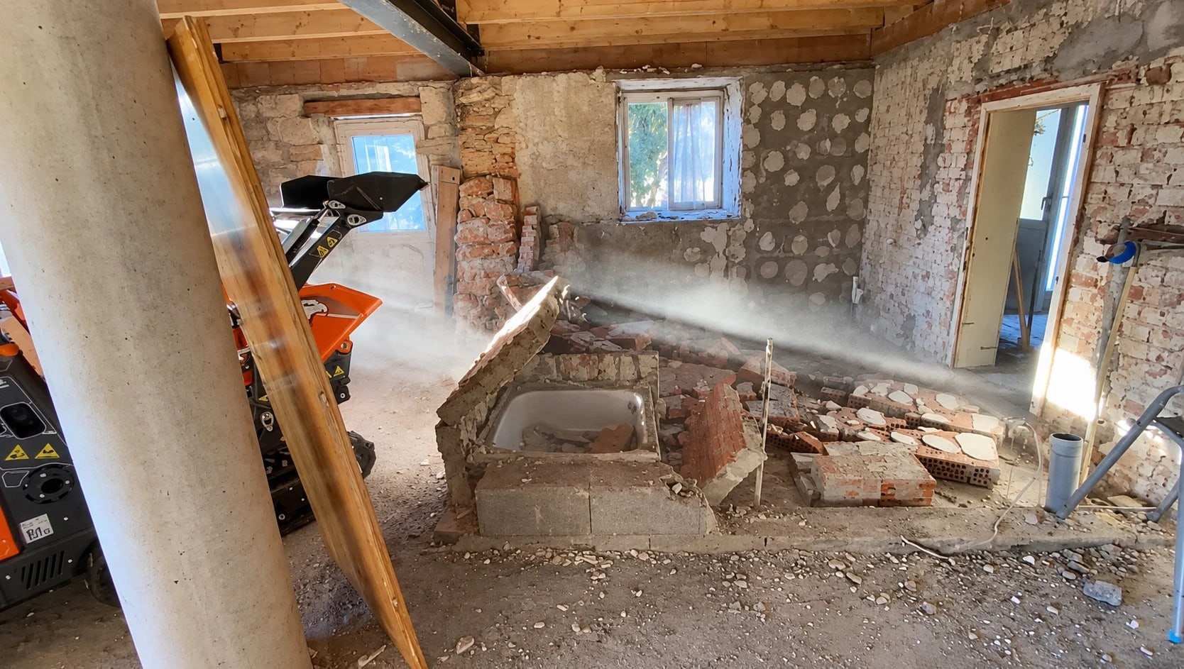 Rückbau in einem Altbau: abgebrochene Ziegelwände rund um eine alte Badewanne, Schutt am Boden, links ein Raupendumper