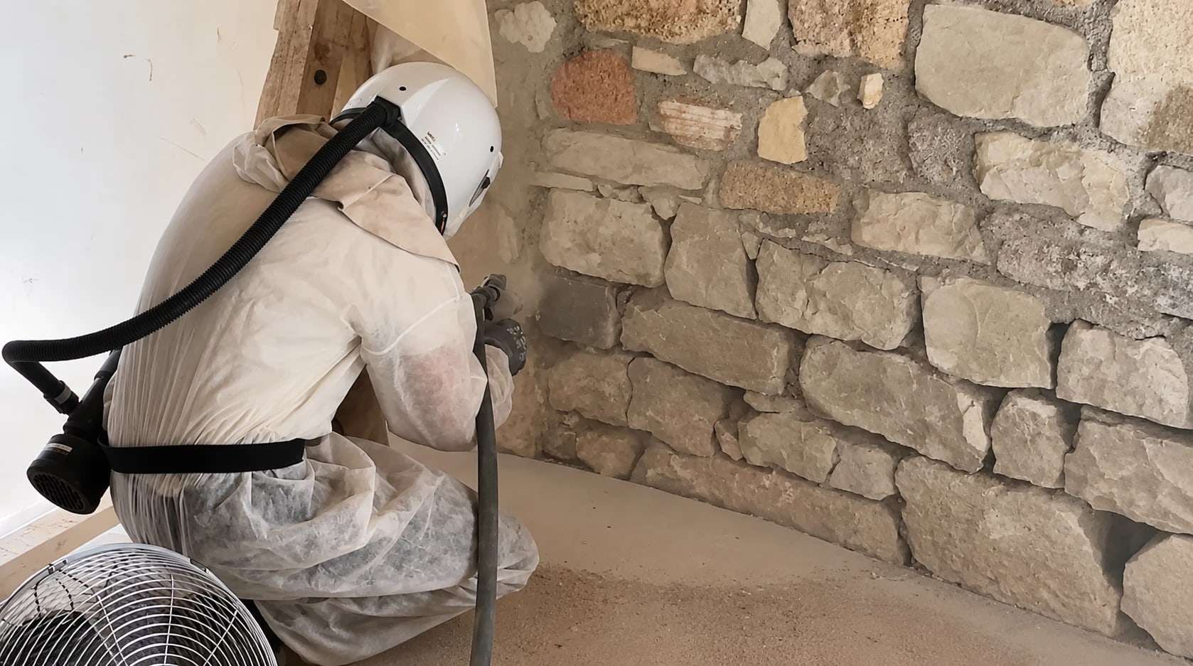 Sandstrahlen einer Natursteinwand im Innenraum, ausgeführt in Schutzanzug mit Atemschutzhelm