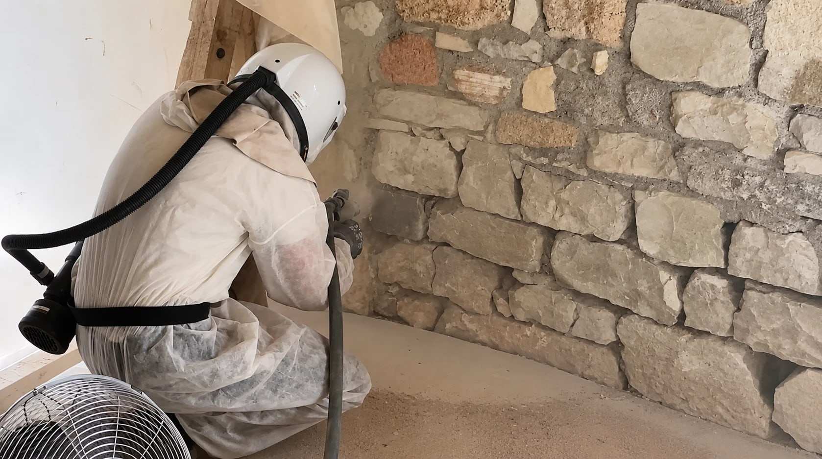 Sandstrahlen einer Natursteinwand im Innenraum, ausgeführt in Schutzanzug mit Atemschutzhelm
